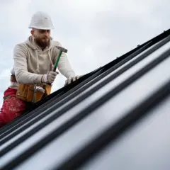 Dekarz w kasku i z młotkiem pracuje na metalowym dachu.
